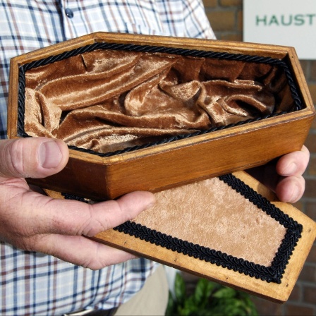Ein Mann hält einen leeren Haustier-Sarg. 