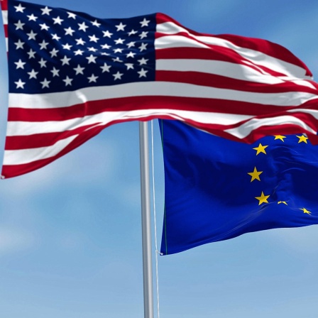 Die Flaggen der EU und der USA flattern vor blauem Himmel.