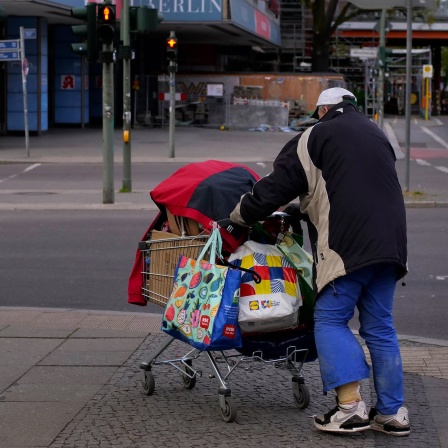 Ein Obdachloser geht im Berliner Stadtteil Steglitz mit seinen Habseligkeiten in einem Einkaufswagen über einen Gehweg.
