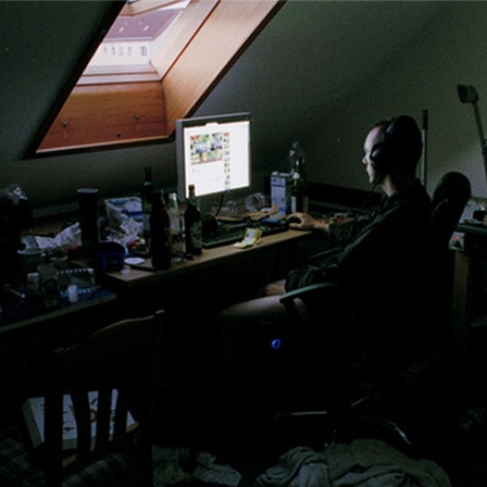 Tino sitzt in seinem dunklen Zimmer vor dem Rechner, von oben fällt Licht durchs Fenster.