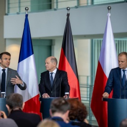 Bundeskanzler Scholz, Frankreichs Präsident Macron und Polens Ministerpräsident Tusk bei einer gemeinsamen Pressekonferenz. Im Hintergrund die jeweiligen Nationalflaggen und die Europa-Flagge. 