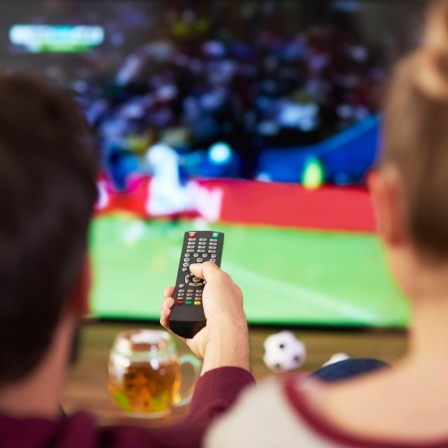Ein Mann und eine Frau gucken gemeinsam Fußball auf dem Fernseher. 
