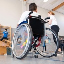 Ein Junge im Rollstuhl und Kinder ohne Behinderung beim Sportunterricht in einer Turnhalle.
      