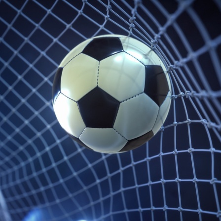Ein Fußball wird bei Dunkelheit im Scheinwerferlicht in ein Tor geschossen.