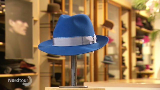 Ein blauer Hut wird in einem Hutladen auf einer Stange präsentiert.