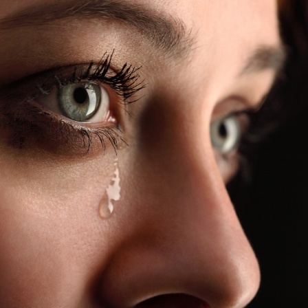 Eine Träne rinnt aus den Auge einer jungen Frau. 