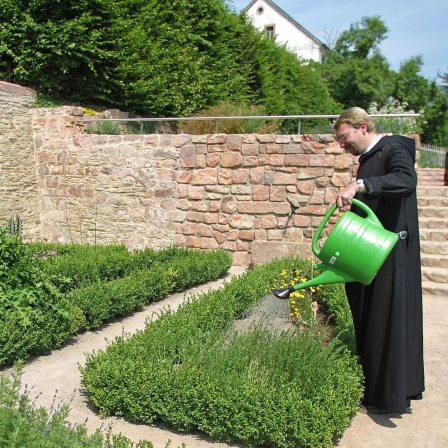 Ein Benediktinermönch gießt die Pflanzen im Kräutergarten eines Klosters.