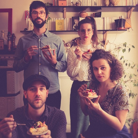 Bandfoto: Die vier Musiker:innen von Nefertiti an der Kaffeetafel