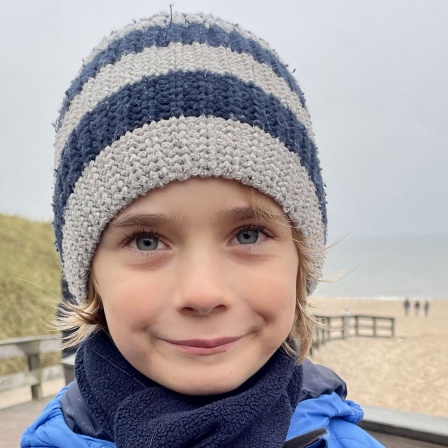 Ein Junge mit Wollmütze steht am Strand.