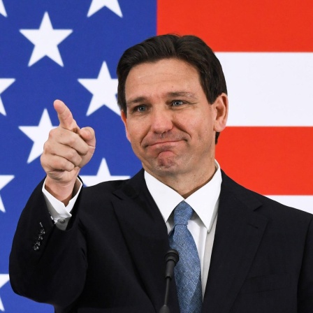Der Gouverneur von Florida, Ron DeSantis, steht vor einer US-Flagge und zeigt nach vorne