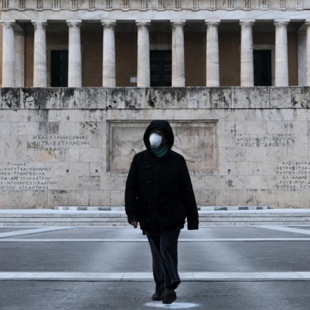 Eine Frau in schwarzer Kleidung trägt eine medizinische Maske und läuft damit über den Syntagma Platz in Athen. Im Hintergrund ist das Grab des Unbekannten Soldaten zu sehen.