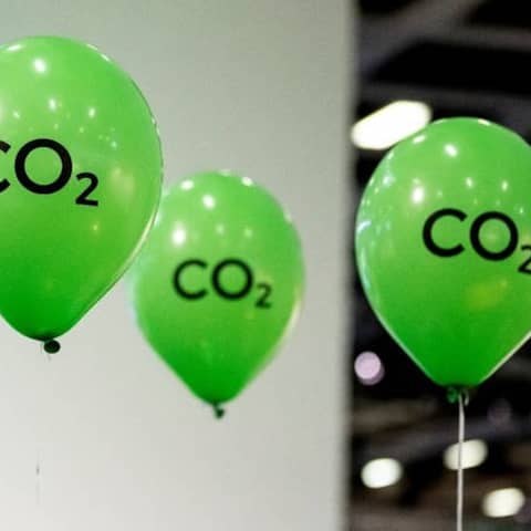 Grüne Luftballons mit der Aufschrift &#034;CO2&#034; schweben an einem Messesstand.