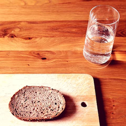 Eine Scheibe Brot und ein Glas Wasser stehen auf einem Tisch.