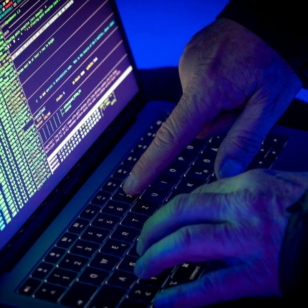 Eine Person in einem dunklen Raum tippt etwas in einen Laptop ein.