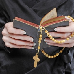 Hände halten Bibel und Rosenkranz