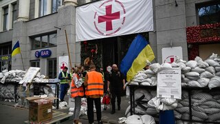 Ukrainische Fahnen sind in der Nähe eines Gebäudes angebracht, vor dem Sandsäcke aufgehäuft stehen.