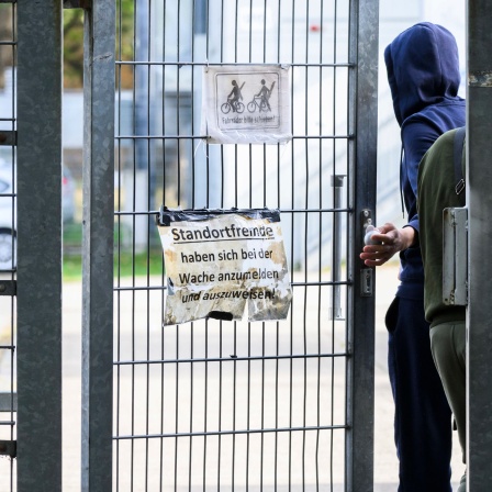 Geflüchteter im Kapuzenpullover geht durch die Tür in einem Gitterzaun der Landesaufnahmebehörde Braunschweig