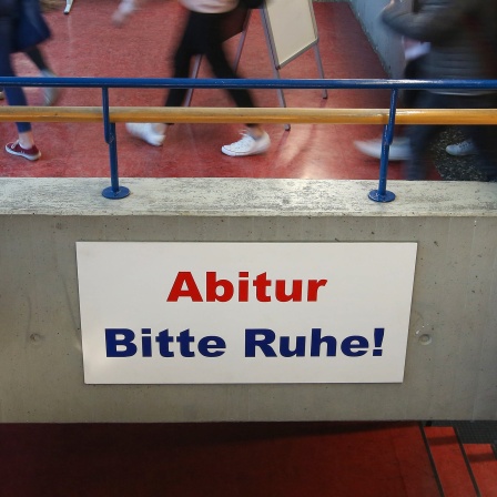 Ein Schild mit der Aufschrift «Abitur Bitte Ruhe!» hängt im Gang eines Gymnasiums, während Schüler vorbeigehen.
