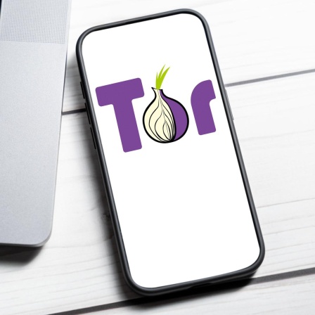 Das Tor-Netzwerk Logo wird auf einem Smartphone-Bildschirm neben einem Laptop angezeigt.