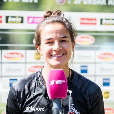 Lena Lotzen hält ein Mikrofon in der Hand und lächelt in die Kamera 