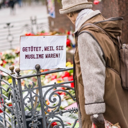 Eine Frau steht auf dem Marktplatz am Denkmal der Brüder Grimm, an dem die Bürger mit Blumen, Plakaten und Kerzen ihre Trauer zum Ausdruck bringen. An einem Plakat steht die Aufschrift "Getötet, weil sie Muslime waren"; © dpa/Frank Rumpenhorst