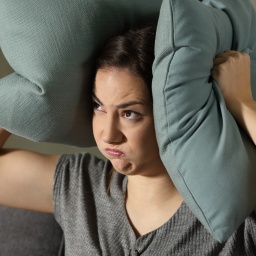 Eine Frau drückt sich gestresst zwei Kissen auf die Ohren.
