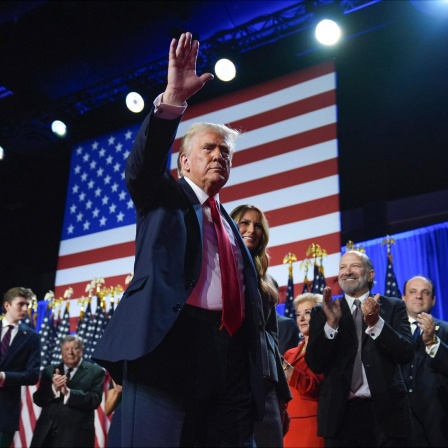 Donald Trump winkt. Hinter ihm stehen seine Frau und andere Menschen. 