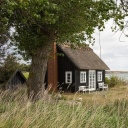 Ein kleines blaues Holzhaus mit zwei weißen Bänken am Strand in Dänemark.