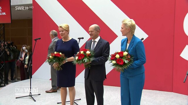 Olaf Scholz (SPD) und zwei Politikerinnen halten je einen Blumenstrauß