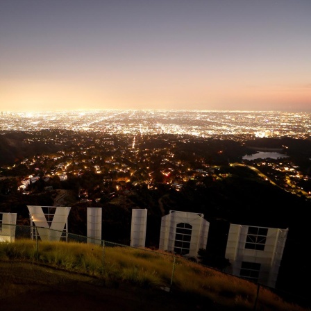 Der ikonische Hollywood-Schriftzug in der Abenddämmerung in der Rückansicht fotografiert mit Blick auf die Lichter von Los Angeles.