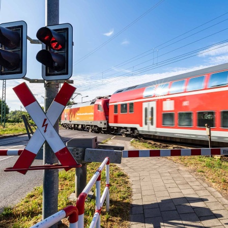 Eine Schranke ist an einem Bahnübergang in Lübbenau geschlossen, wärend ein Regionalzug vorbeifährt.
