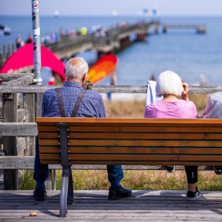 Drei Senioren sitzen auf einer Bank an der Seebrücke.