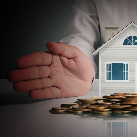 Ein Miniaturhaus und Geld im dunklen Lichteinfall.