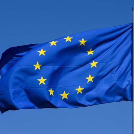 Kiel, eine im Wind wehende Flagge der Europaeischen Union mit den 12 fünfzackigen, gelben Sternen auf azurblauem Hintergrund vor blauem Himmel.