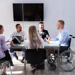 Mann im Rollstuhl sitzt mit seinen Kollegen in einer Besprechung