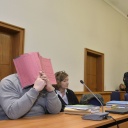 Niels H. sitzt vor Gericht auf der Anklagebank und hält sich eine Mappe vor das Gesicht und ist von Pressevertretern umringt.