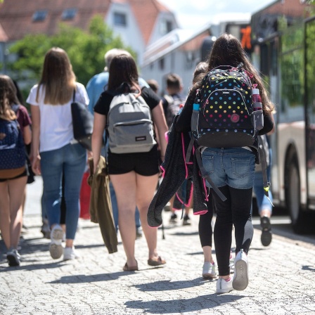 Schülerinnen gehen an einer Bushaltestelle zu wartenden Bussen