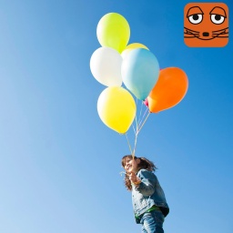 Mädchen hält vor blauem Himmel mehrere bunte Luftballons in der Hand