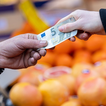 Ein Kunde bezahlt seinen Einkauf an einem Stand auf einem Wochenmarkt mit einem Fünf-Euro-Schein (gestellte Szene).