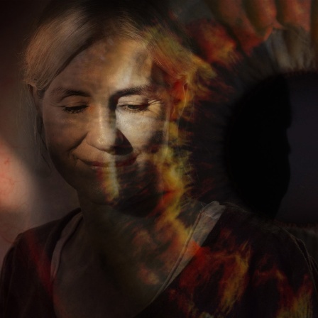 Eine Frau steht mit geschlossenen Augen im Licht, dass durch eine Öffnung scheint.