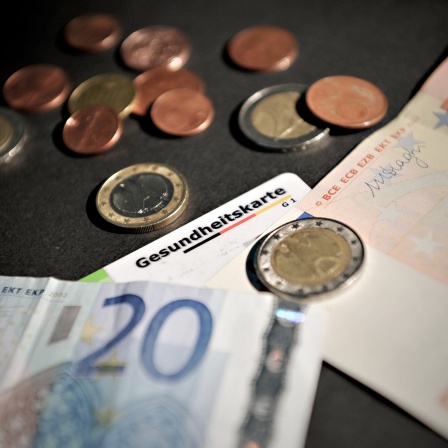 Ein Teil einer Gesundheitskarte ist zwischen Euro-Noten und Münzen zu sehen.