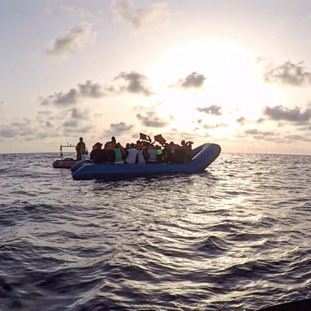 Symbolbild: Seenotretter:innen schauen zu einem Schlauchboot mit Flüchtlingen (2020).