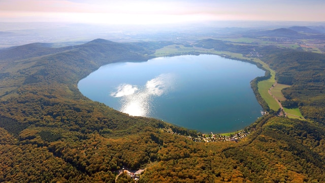 Blick auf den Laacher See bei Bell in Rheinland-Pfalz. Dieser wird umgeben von Wäldern. Im Bild scheint die Sonne.
