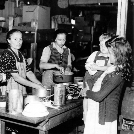 Frauen bereiten 1948 an einem Tisch im bayerischen Flüchtlingslager Allach Mahlzeiten zu (undatierte Aufnahme von 1948)
