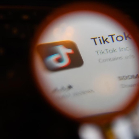 Die App Tik Tok auf einem Smartphonebildschirm durch eine Lupe gesehen.