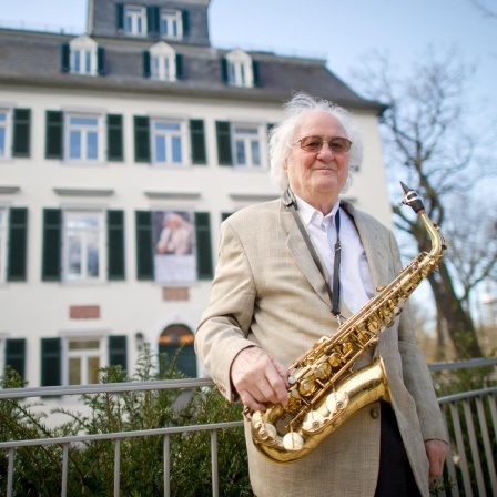 Emil Mangelsdorff steht mit einem Saxophon am Zaun vor einer Villa
