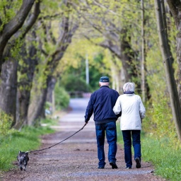 Eine Frau und ein Mann, beide im Rentenalter, gehen mit ihrem Hund spazieren.