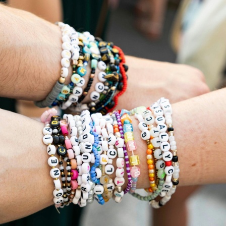 Zwei Taylor Swift-Fans halten ihre Arme mit den typischen Swiftie-Armbändern in die Kamera.