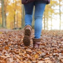 Frau mit Stiefeln spaziert durch Herbstlaub, das auf dem Waldboden liegt.