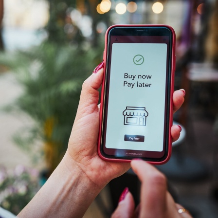 Eine Frau hält ein Handy in der Hand. Auf dem Bildschirm steht auf englisch: Buy now, pay later